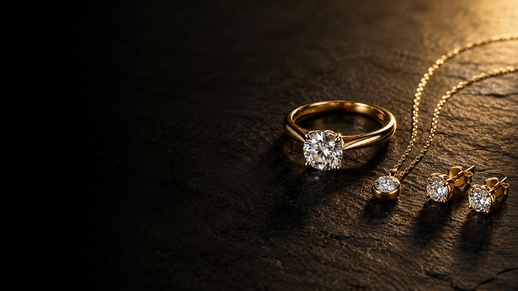 A gold diamond solitaire ring, pendant and stud earrings arranged on black marble under a single warm light